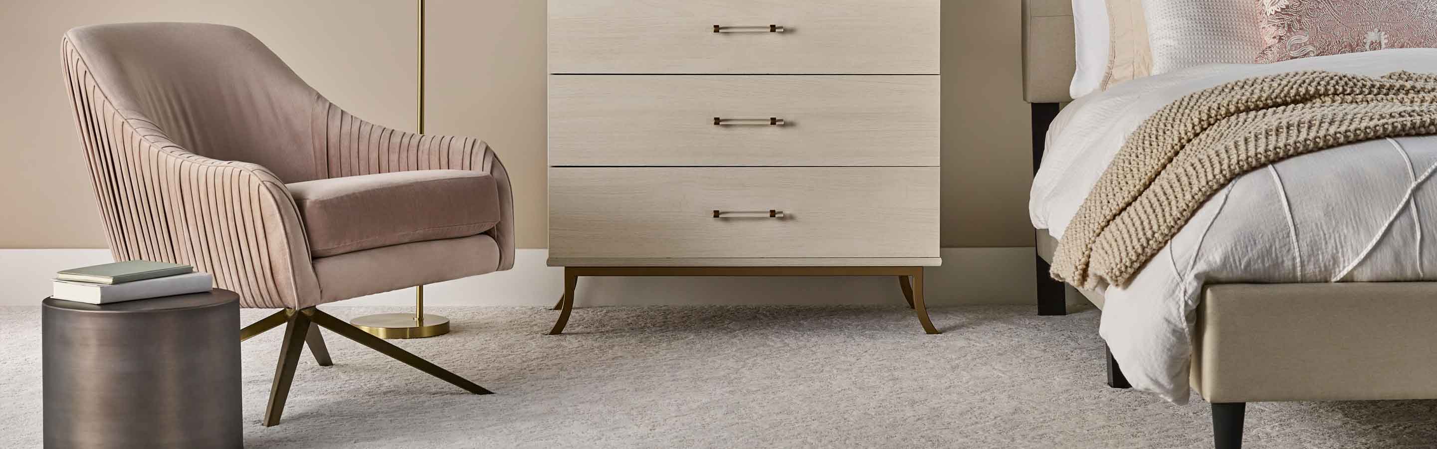 modern bedroom with pink chair,  cream colored dresser, and pink accents, beige textured carpet